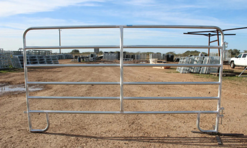 A sturdy metal gate stands open on a dirt path under a blue sky. The area is filled with stacks of similar gates and a white truck is in the background.